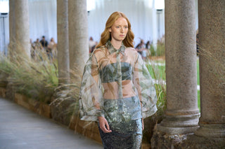 Woman in a stylish outfit standing in an outdoor setting with columns and greenery.