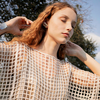 woman with long red hair and a meshed blouse over a top, with silver earrings and bracelet