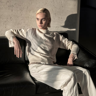 woman sitting on the sofa wearing an argyle sweater and white denim jeans