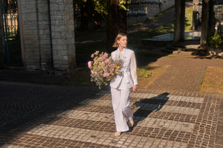 Woman white dressed with shirt, waistcoat, trousers, flat sandals and flowers on hand
