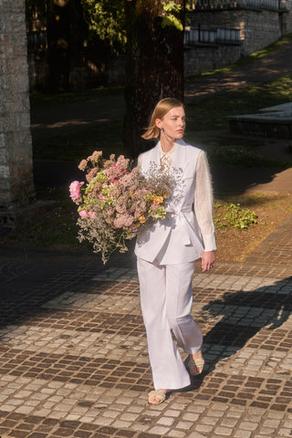 Woman white dressed with shirt, waistcoat, trousers, flat sandals and flowers on hand